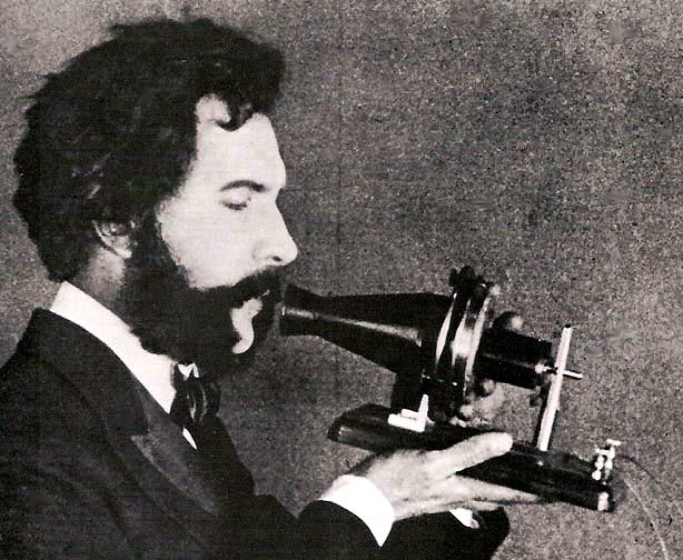 An actor portraying Alexander Graham Bell speaking into a early model of the telephone for a 1926 promotional film by AT&T, public domain. The phone is a simple conical part  in which the actor is speaking, attached to a piece of wood, with no ear piece at all